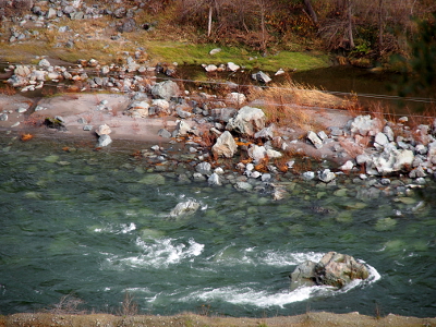 [A path of small boulders leads into the river where some lie at the edge while others are submerged but still visible through the clear water.]